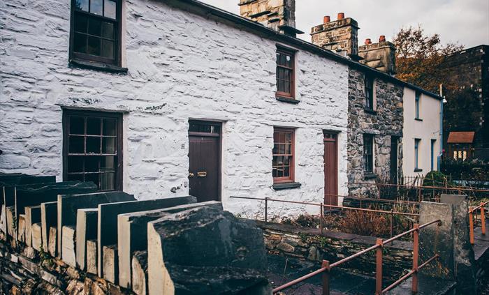 A row of 4 small cottages, built of stone. The first two cottages are painted white. They have one window and a door downstairs and one window upstair